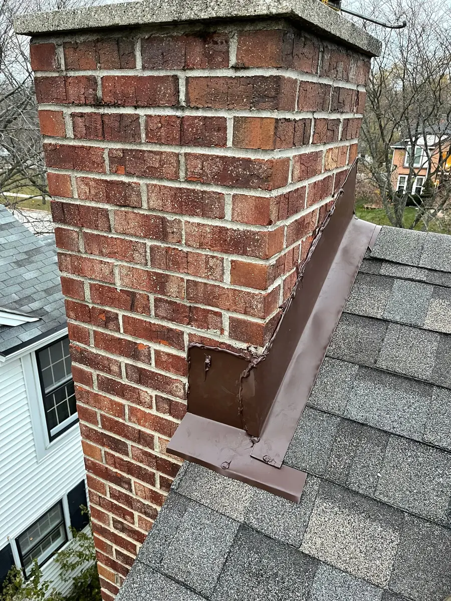New brown metal step flashing running up the side of a brick chimney over new shingles