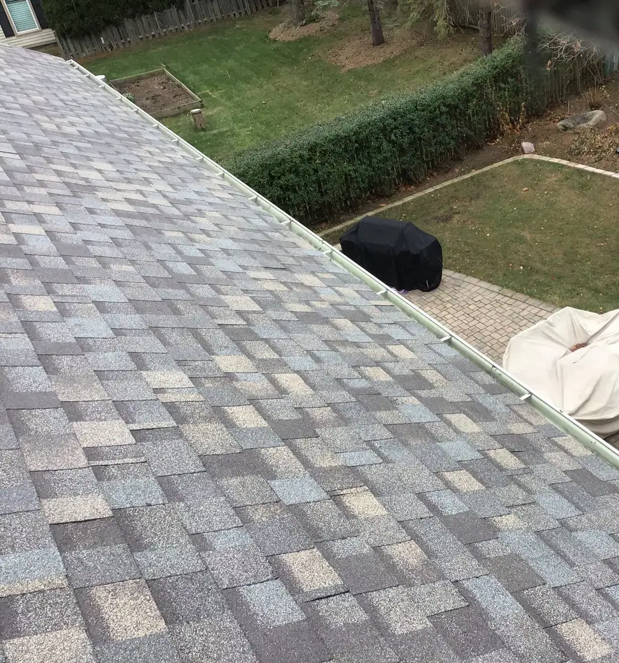 New architectural shingles running down to a white aluminum gutter above a backyard patio