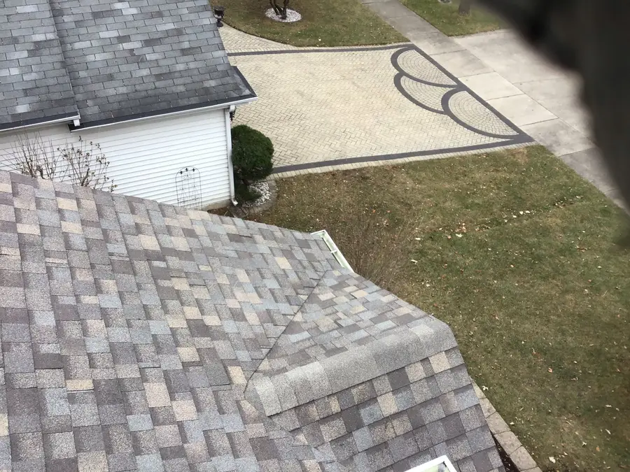 Finished gray and tan architectural shingle roof edge above a backyard with a lawn and paver path