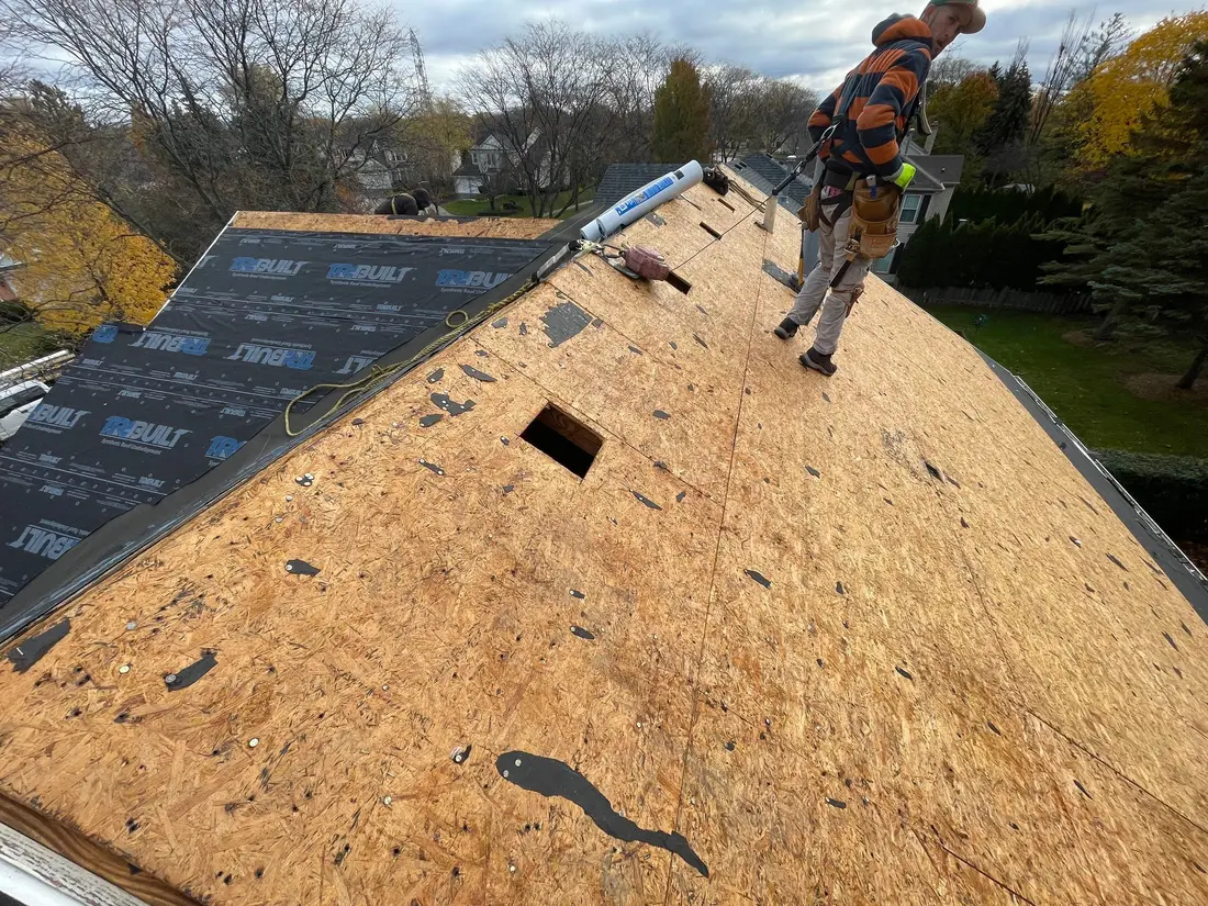 Roofer in a safety harness tied off to a rope walking across a bare roof deck during a tear-off
