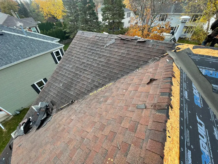 Faded reddish brown shingles on one slope next to fresh synthetic underlayment on the next during a replacement