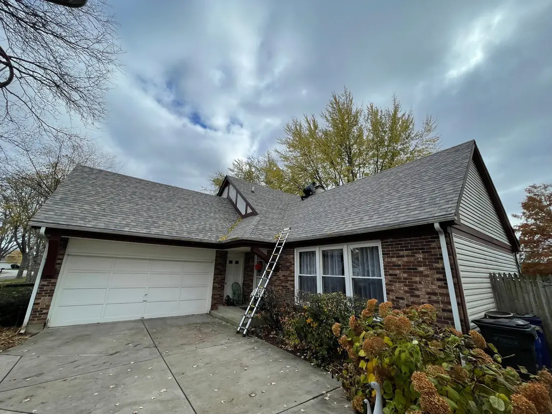 Ranch house with a new gray roof, a white garage door and a ladder leaning on the front wall
